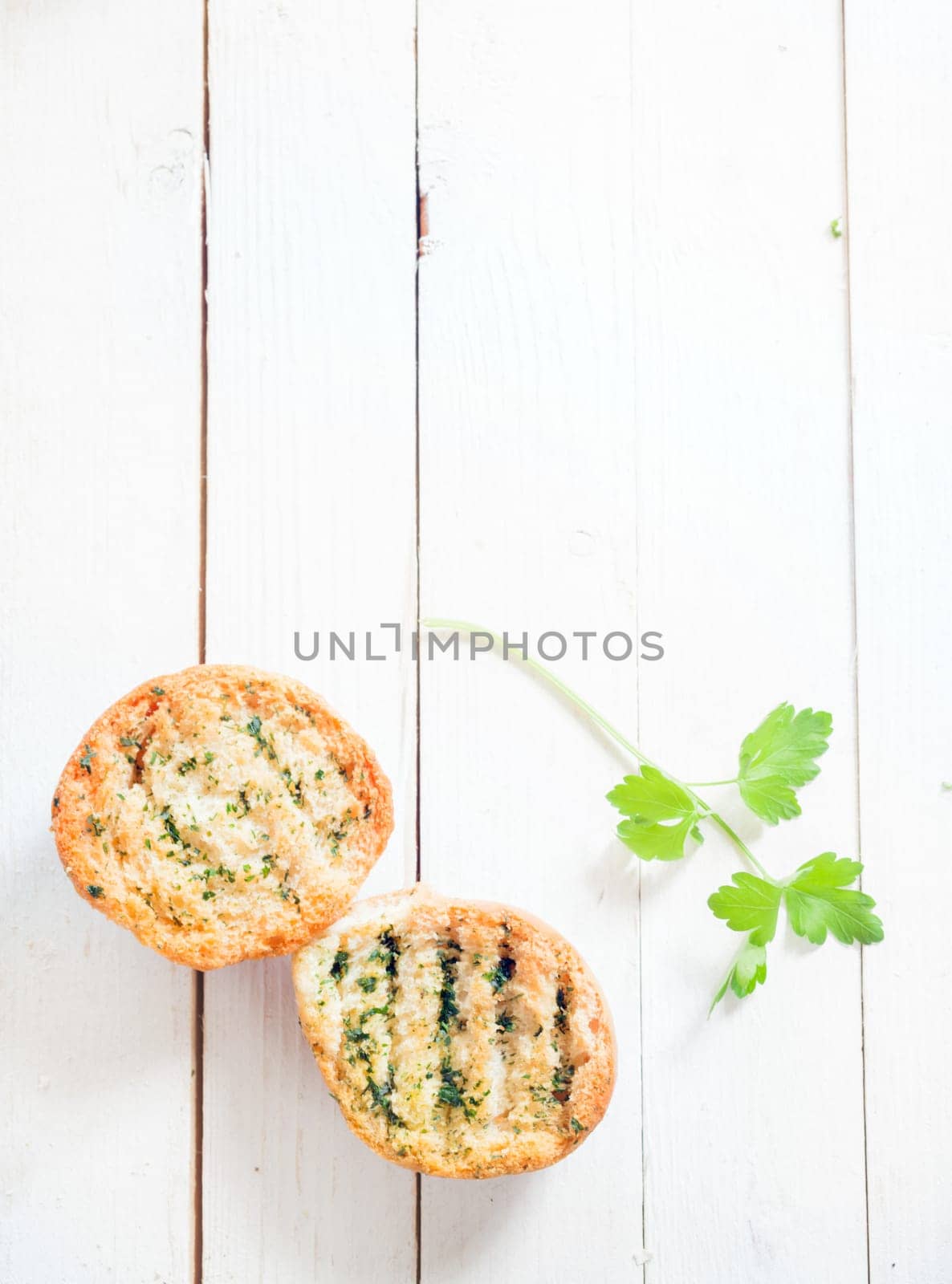 Grilled crusty crisp herb bread on a white wooden table with a sprig of fresh parsley, overhead view with copyspace