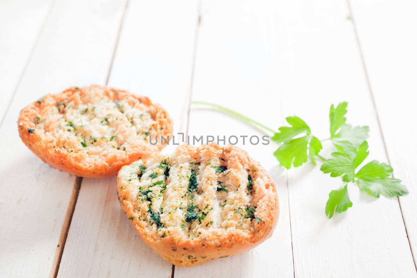 Delicious grilled golden crisp herb bread with fresh parsley on a white wooden garden table, low angle view