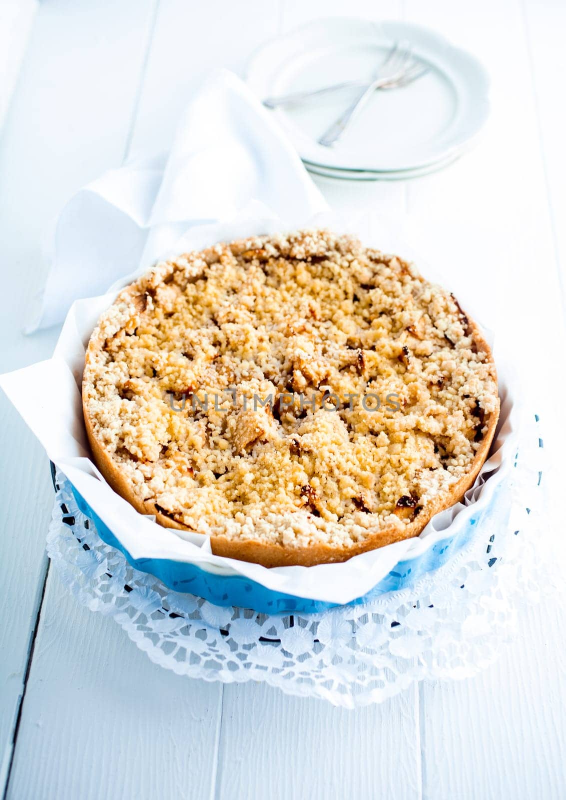 High key image of a delicious fresh baked plum pie on a decorative doily on white boards with plates ready to be served