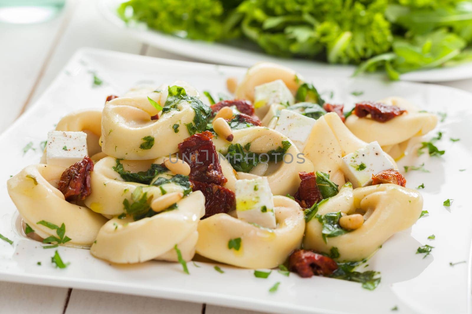 Stuffed Italian tortellini pasta noodles with feta cheese, fresh basil and pine nuts served with a leafy green salad