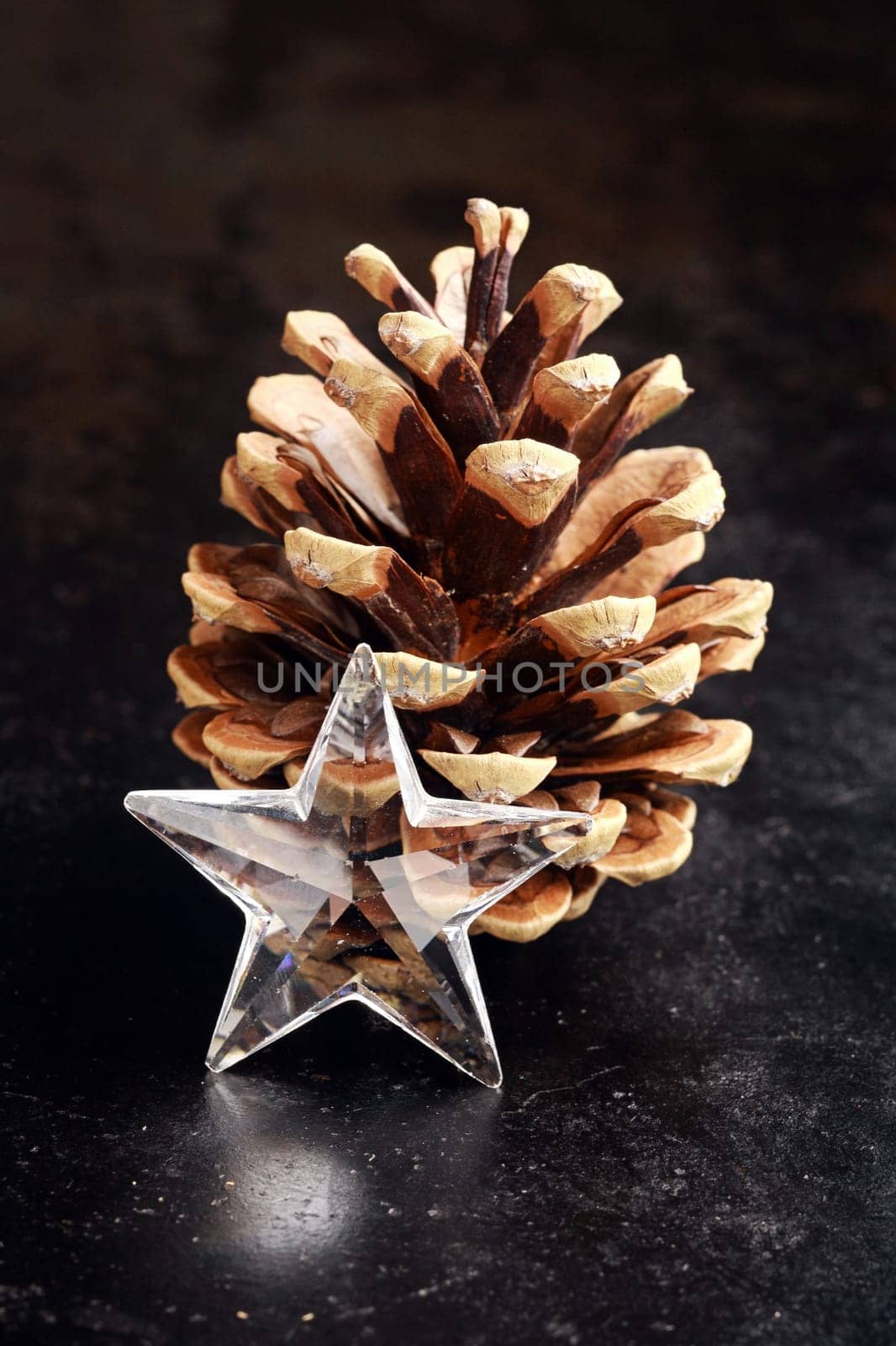 Christmas background with a faceted transparent star decoration and pine cone on a reflective dark surface with copyspace for your seasonal greeting