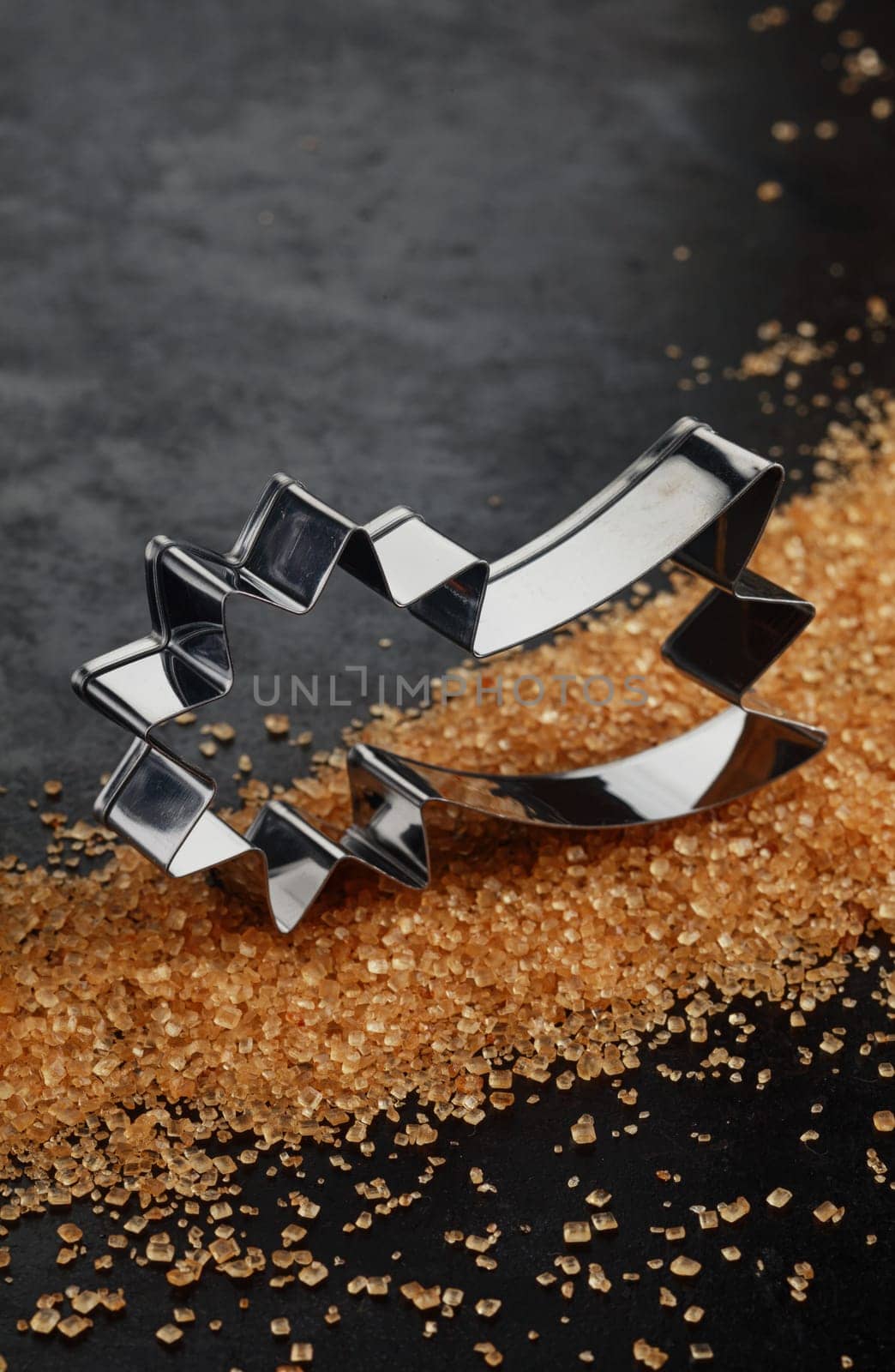 Shiny aluminium shooting star Christmas cookie cutter on a bed of caramelized brown sugar crystals on a dark background with copyspace for your seasonal greeting