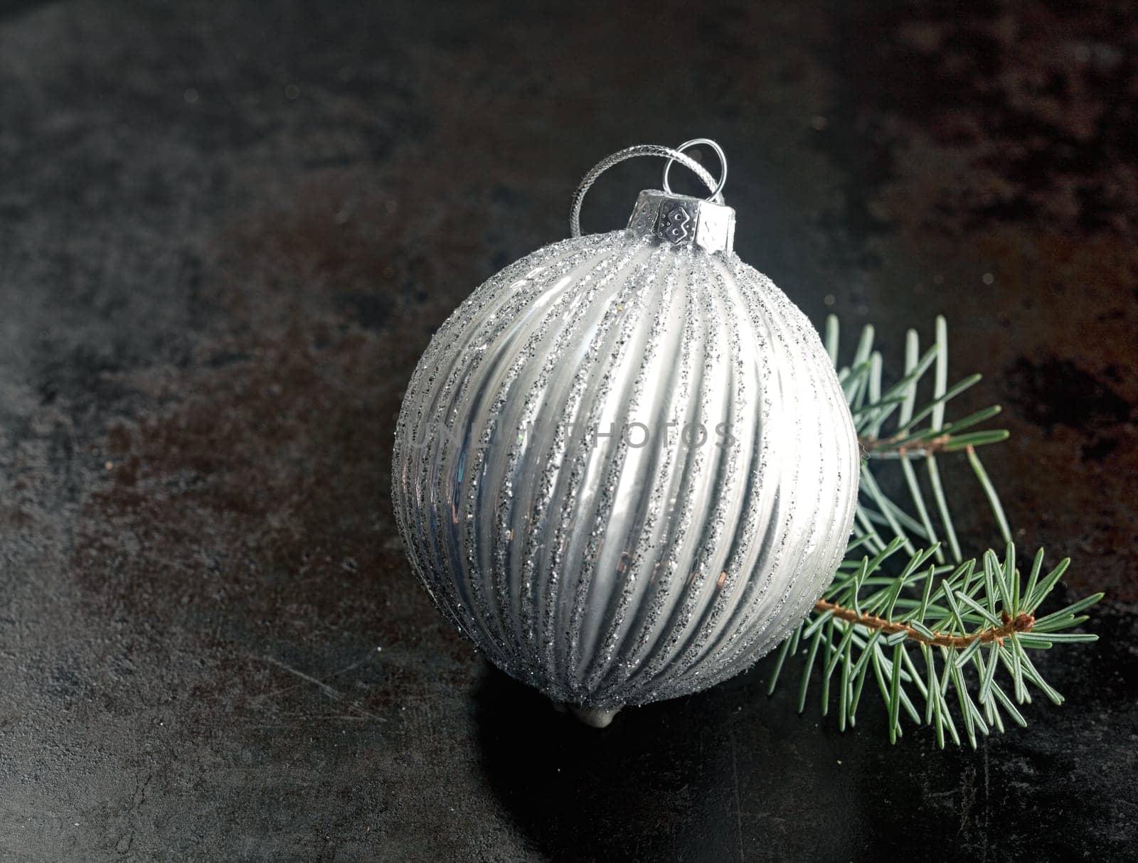 Silver bauble Christmas decoration with a ridged pattern with a twig of pine needles on a dark background with copyspace for your seasonal message
