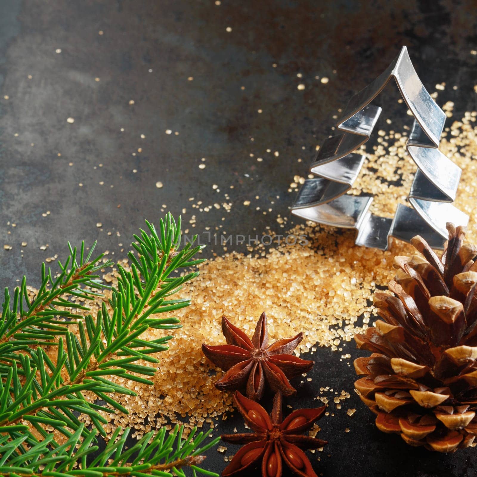Christmas greeting card background with a cookie cutter in the shape of a Christmas tree with a pine branch, cone, caramelized brown sugar and star anise spice on a dark background with copyspace
