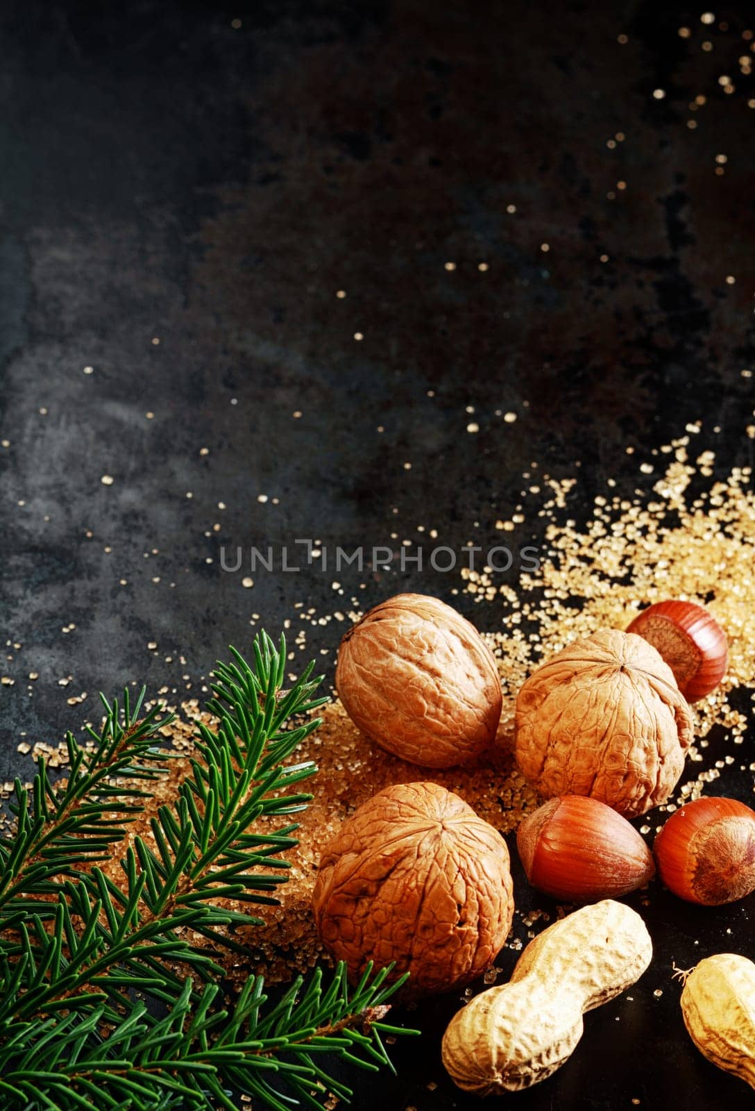 Traditional Christmas nuts with whole almonds, hazelnuts and peanuts in their shells on a dark background with scattered sugar crystals and pine foliage , with copyspace