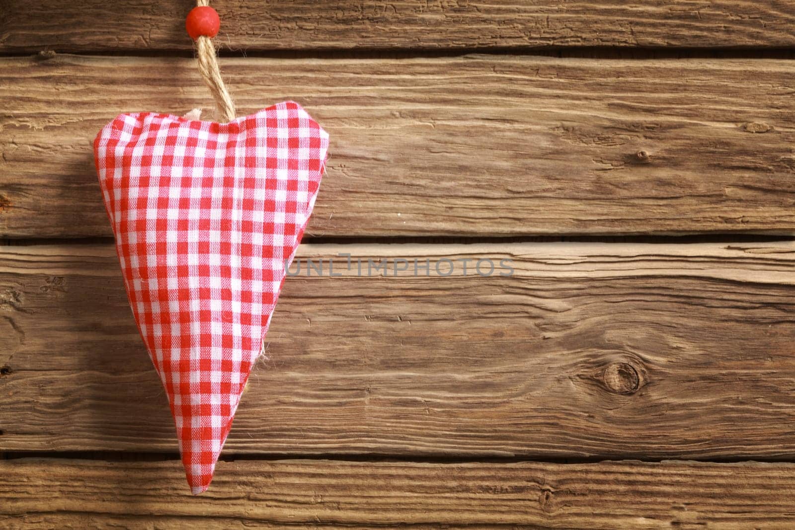 Handmade rustic hanging red and white checked heart ornament for Christmas or Valentines Day for a sweetheart or loved one with copyspace on a wooden background