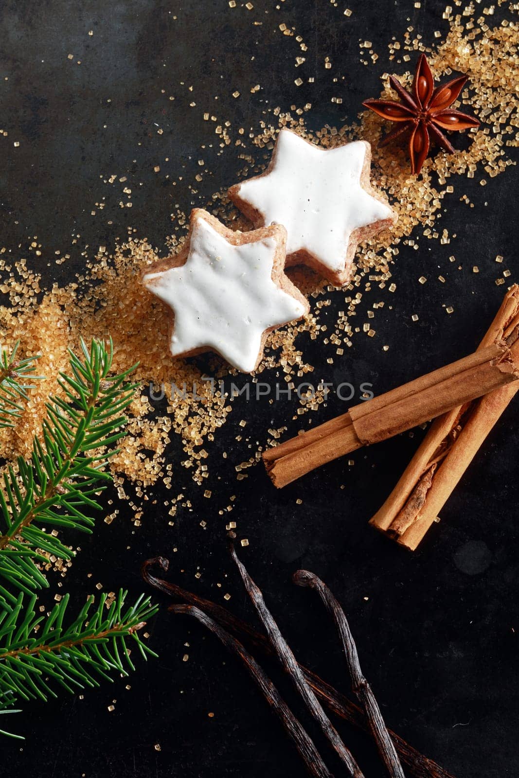 Christmas food still life with copyspace for your seasonal greeting with an overhead view of glazed white star shaped cookies, vanilla pods, stick cinnamon and sugar on a dark background