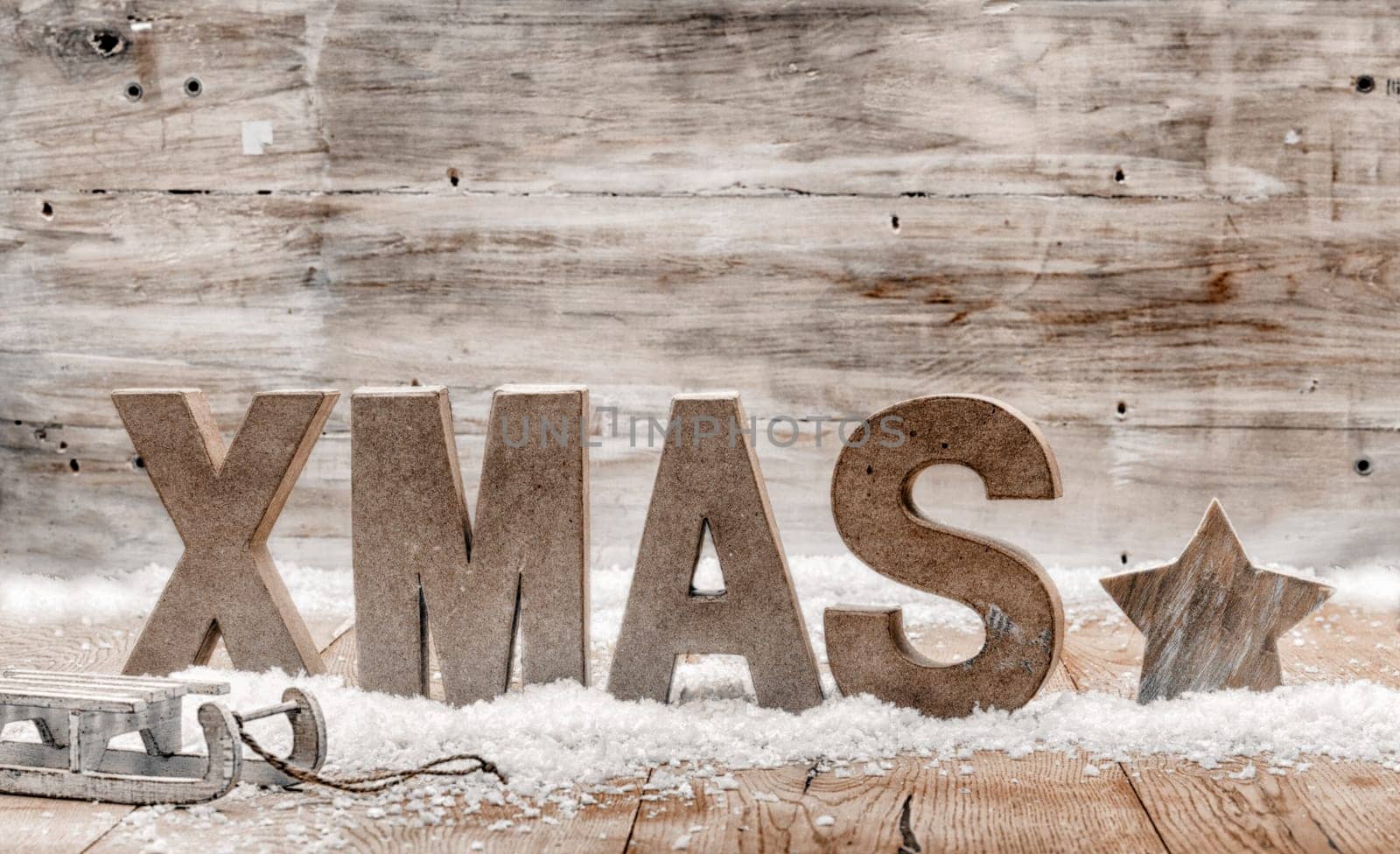 Wood craft rustic Christmas background with wooden letters spelling Xmas standing in snow with a star and small kids sleigh or toboggan against a weathered wooden wall with copyspace for your greeting