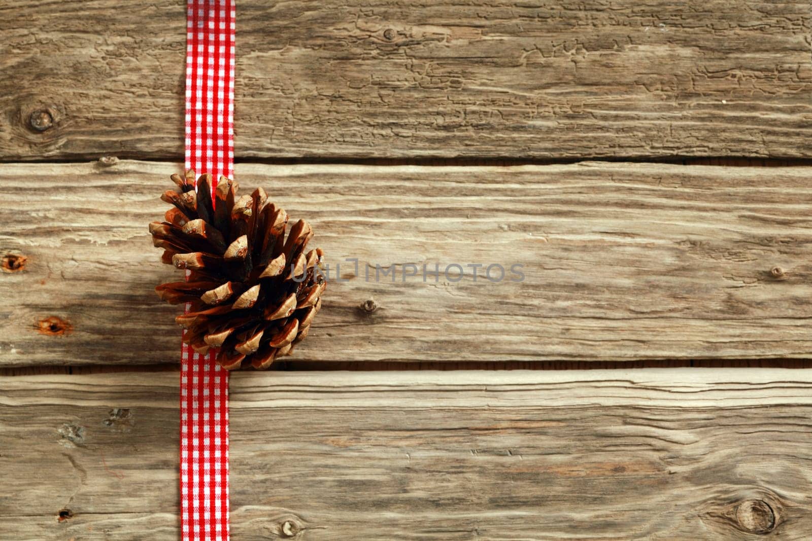 Rustic Christmas background with a decorative white end red checked ribbon and pine cone on wooden boards with copyspace for your seasonal message or greeting