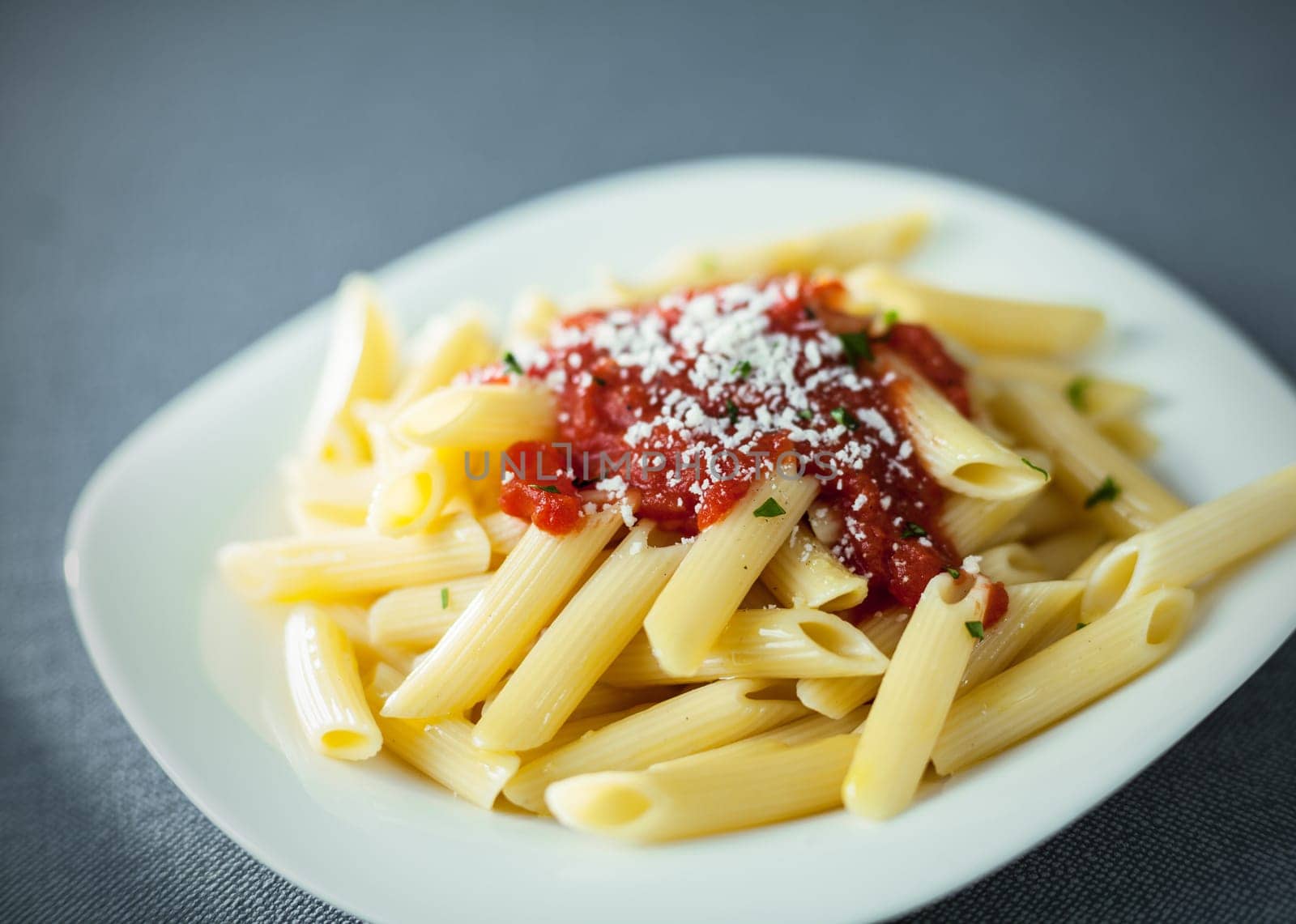 Serving of traditional cooked penne rigate pasta topped with a spicy tomato sauce topped with grated parmesan cheese