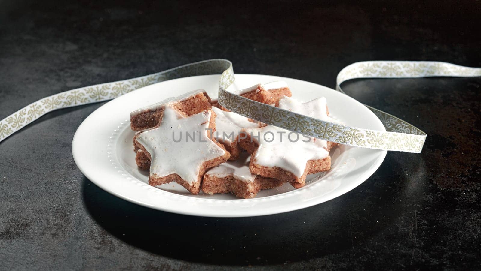 Plate of traditional Christmas cookies in the shape of a white glazed star with a decorative silver ribbon for a festive holiday background