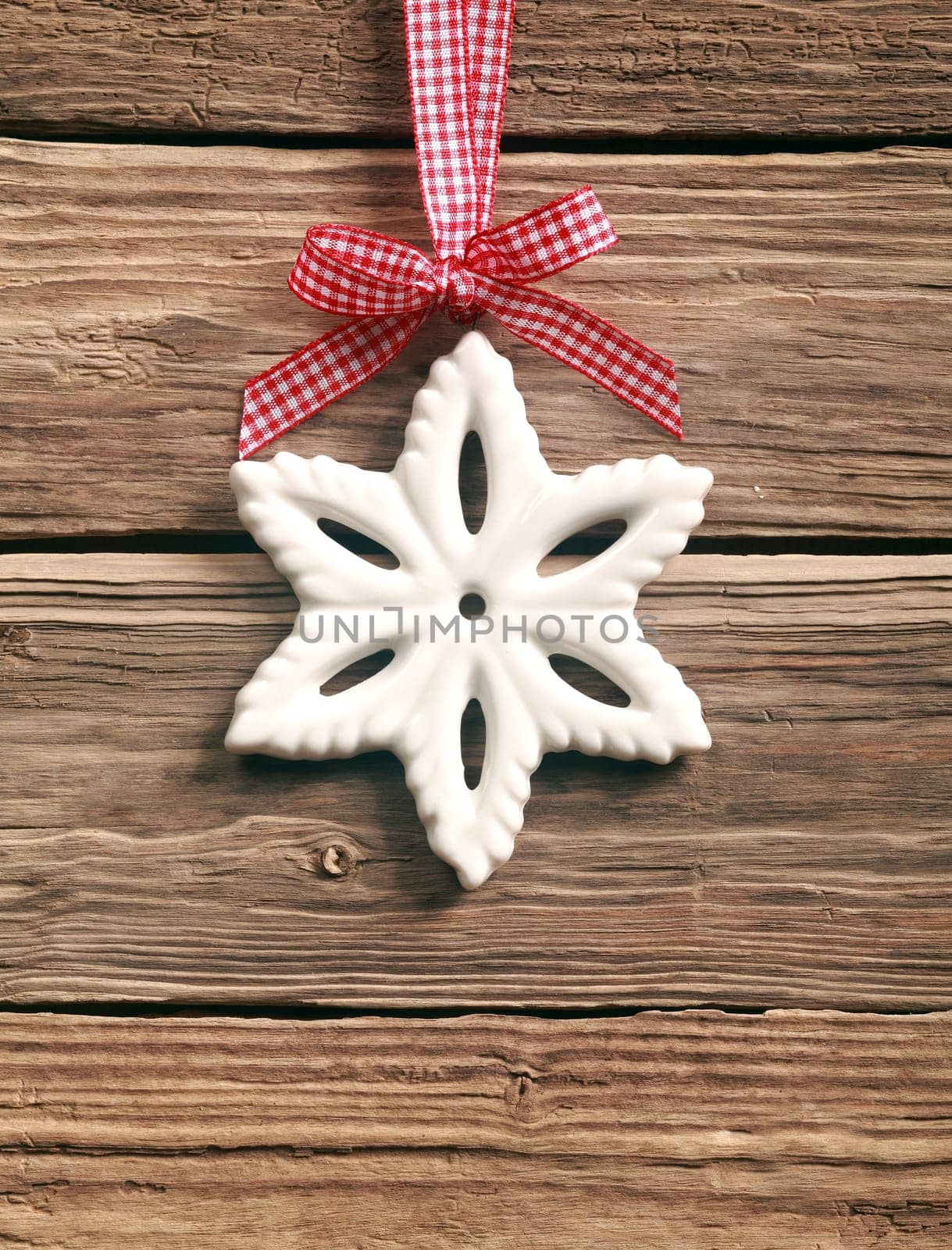 Rustic Christmas background with a white wintry snowflake decoration hanging on a red and white ribbon tied in an ornamental bow, on wooden boards with copyspace
