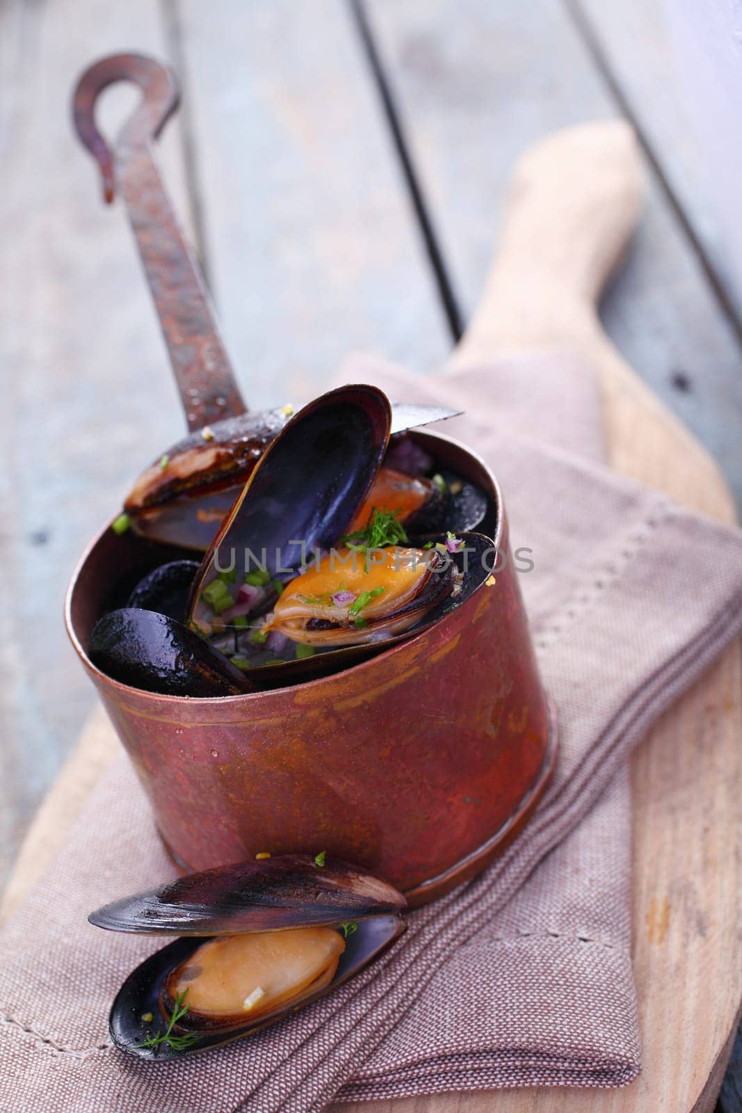 Serving of delicious gourmet freshly steamed marine mussels in a copper pot with an open one displayed below on a napkin in a rustic kitchen