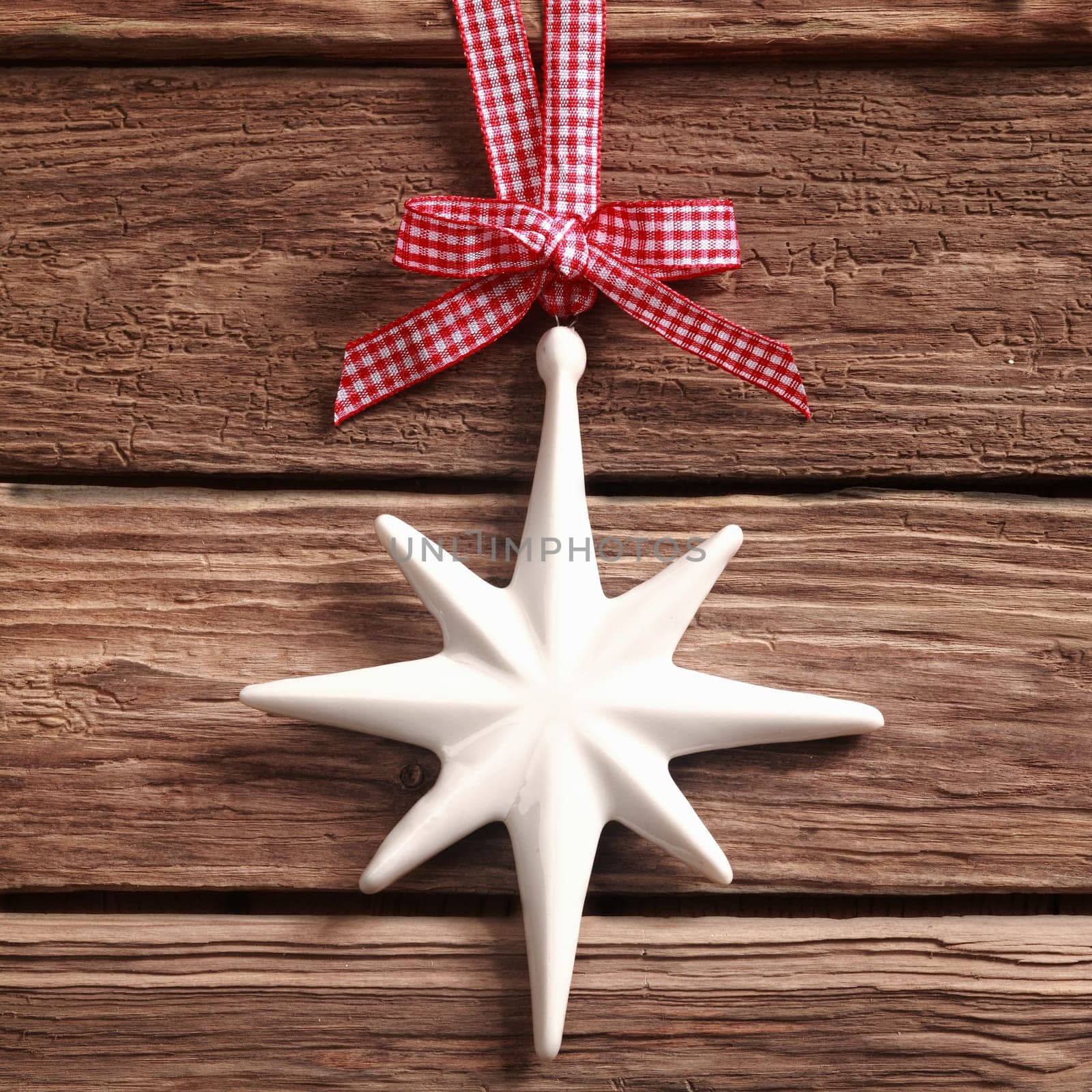 White Christmas star ornament hanging from a pretty red and white checked ribbon and bow on rustic textured wood in square format