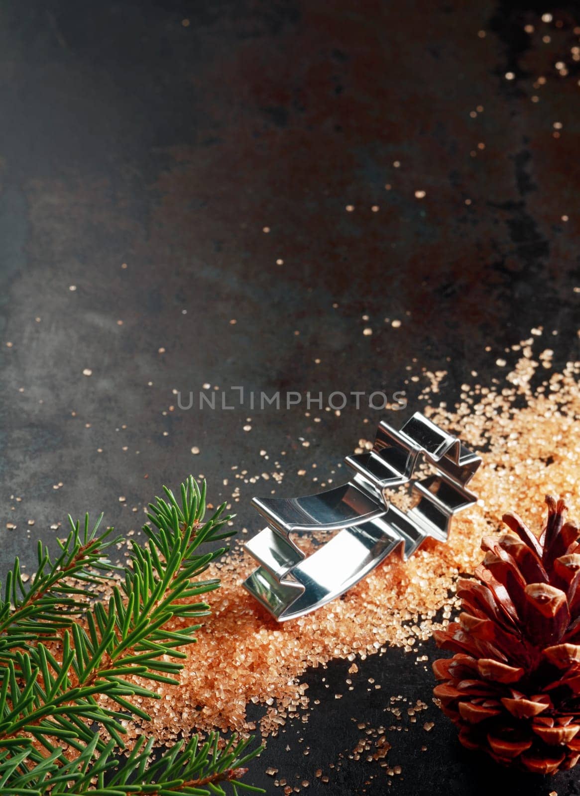 Christmas baking still life with a star shaped cookie cutter and caramelized sugar on a dark background with a decorative pine cone and fresh green pine branch, with copyspace in vertical format
