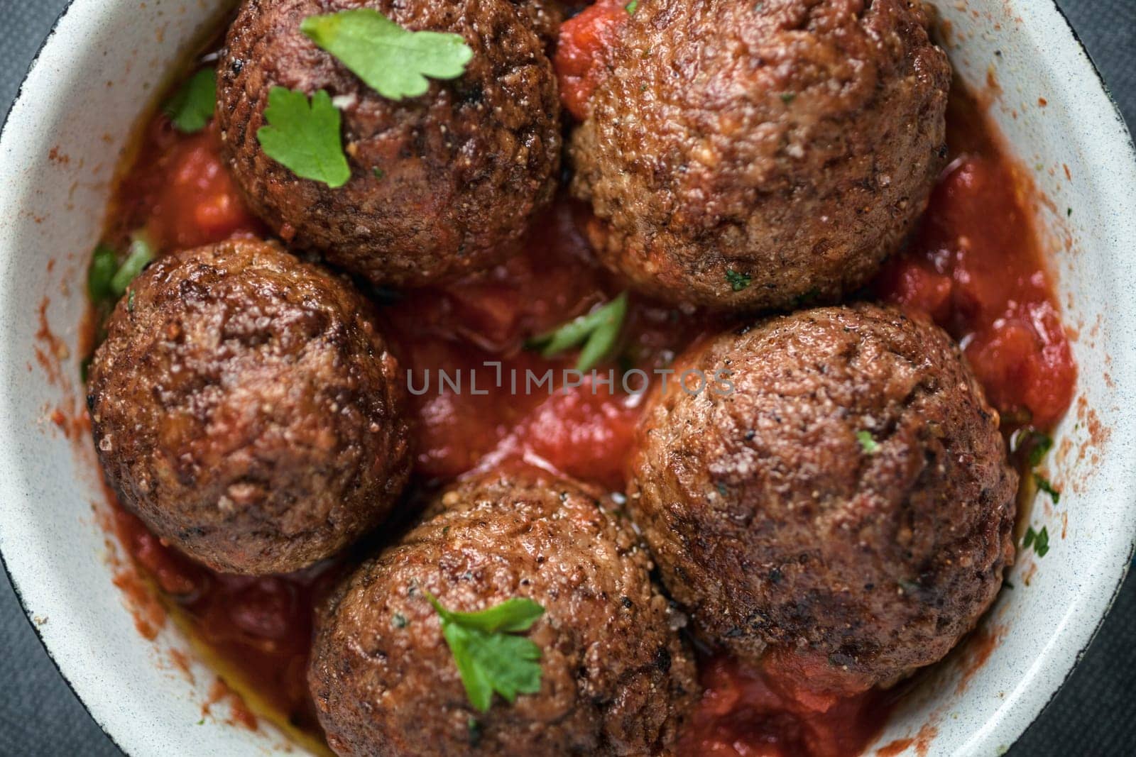 Serving of delicious seasoned meatballs in tomato sauce garnished with fresh herbs, overhead view in a saucepan