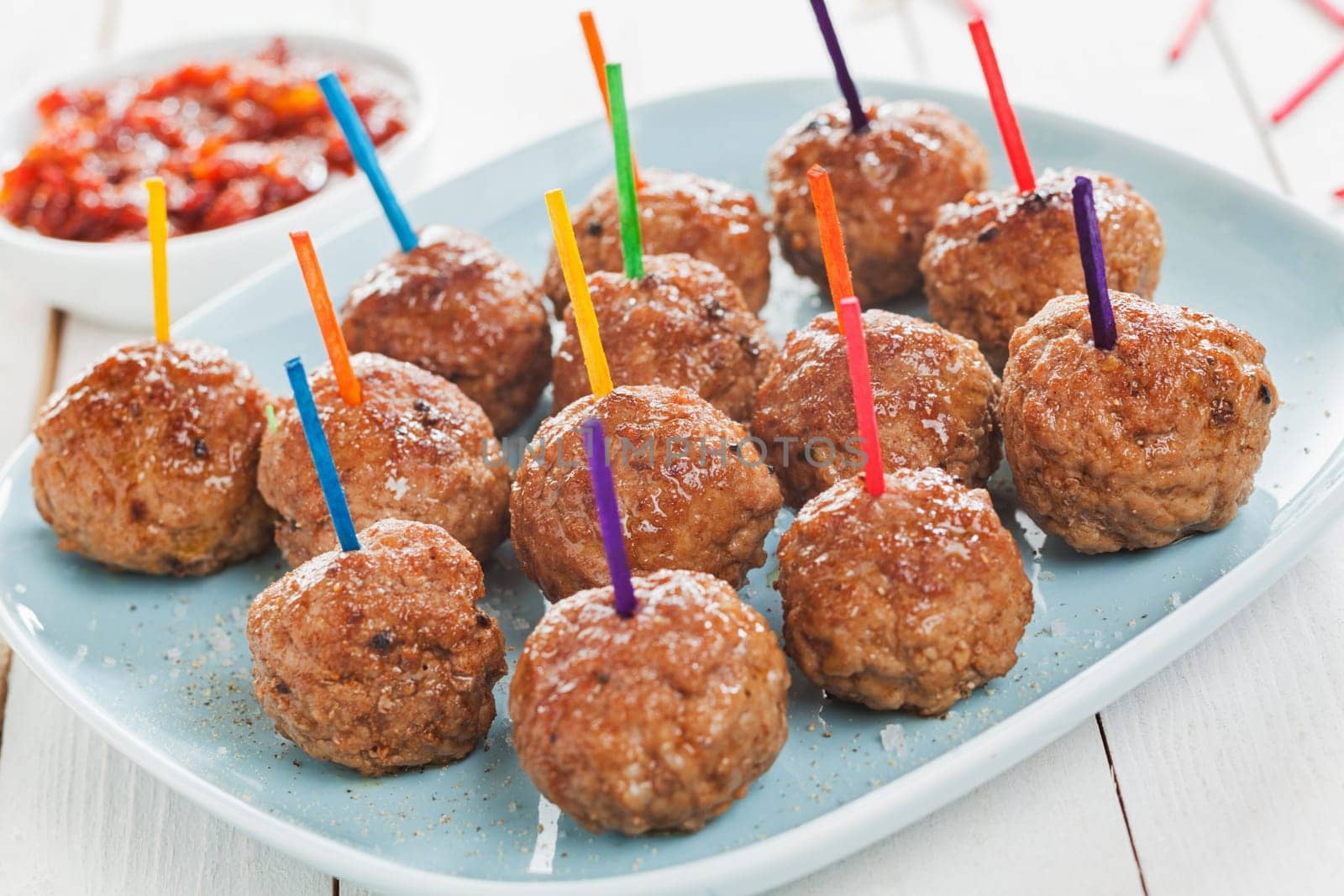 Buffet display of tasty spicy meatballs with colorful toothpicks for dipping arranged on a plate
