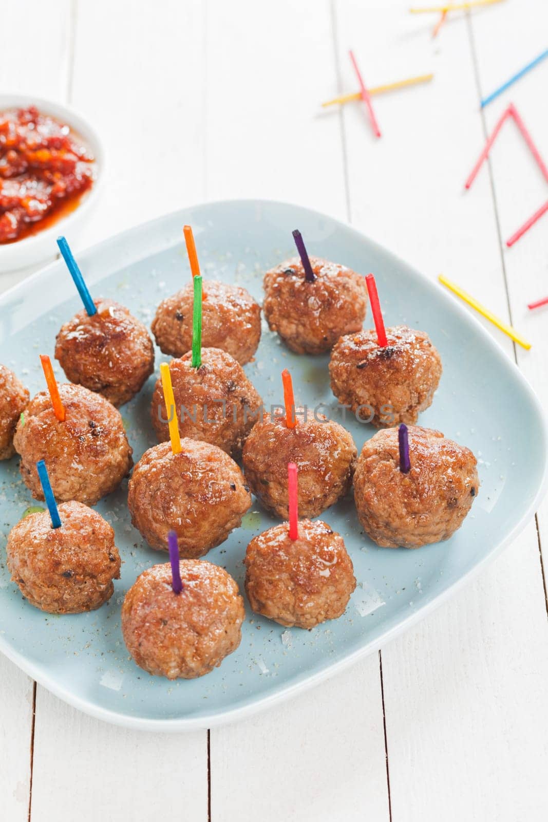 Preparing a tray of delicious spicy seasoned meatballs with colored toothpicks for snacks at a catered event , high angle view on a plate on rustic white boards