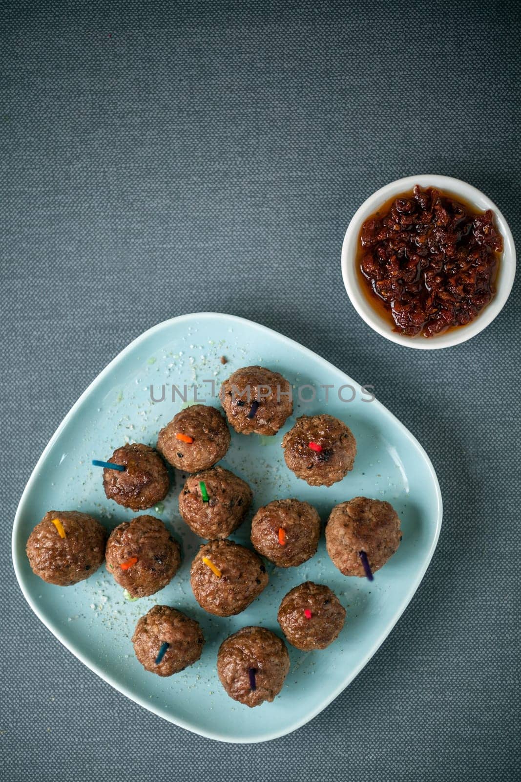 Overhead view of a plateful of seasoned meatballs and savory spicy tomato and chili pepper dip for appetizers, overhead view on a grey tablecloth with copyspace