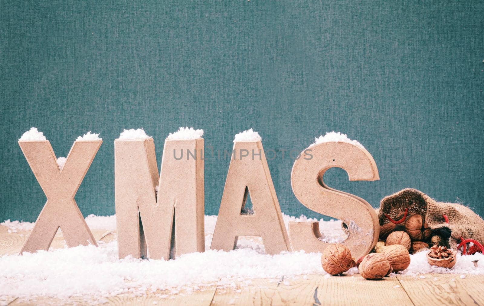 Cool winter Xmas background with white alphabet letters standing in white winter snow with walnuts in their shells spilling from a hessian bag against blue with copyspace for your Christmas greeting