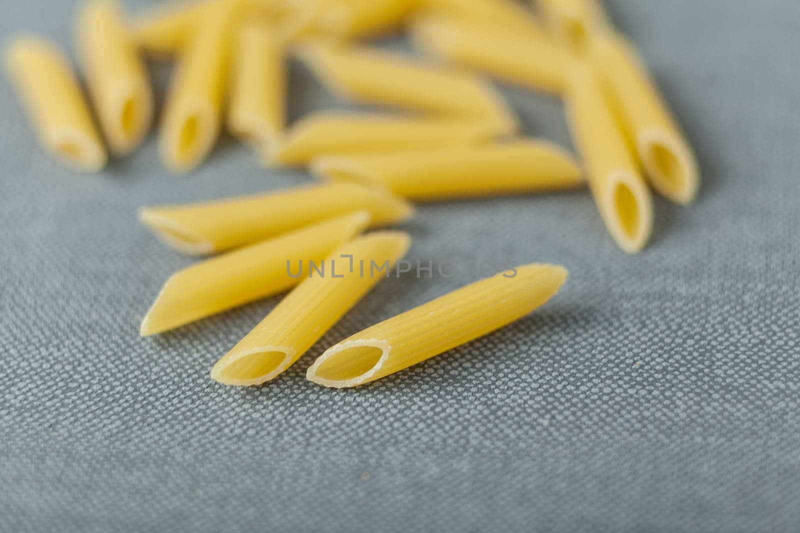 Scattered dried penne rigate Italian pasta with its ridged tubes to assist in the adherence of sauces and toppings, low angle on a grey textile with copyspace