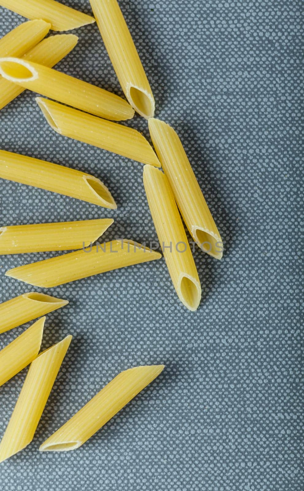 Dried Italian penne rigate pasta with its distinctive angle cut tubular shape and ridges for aiding the adhesion of sauces on a grey textile background with copyspace