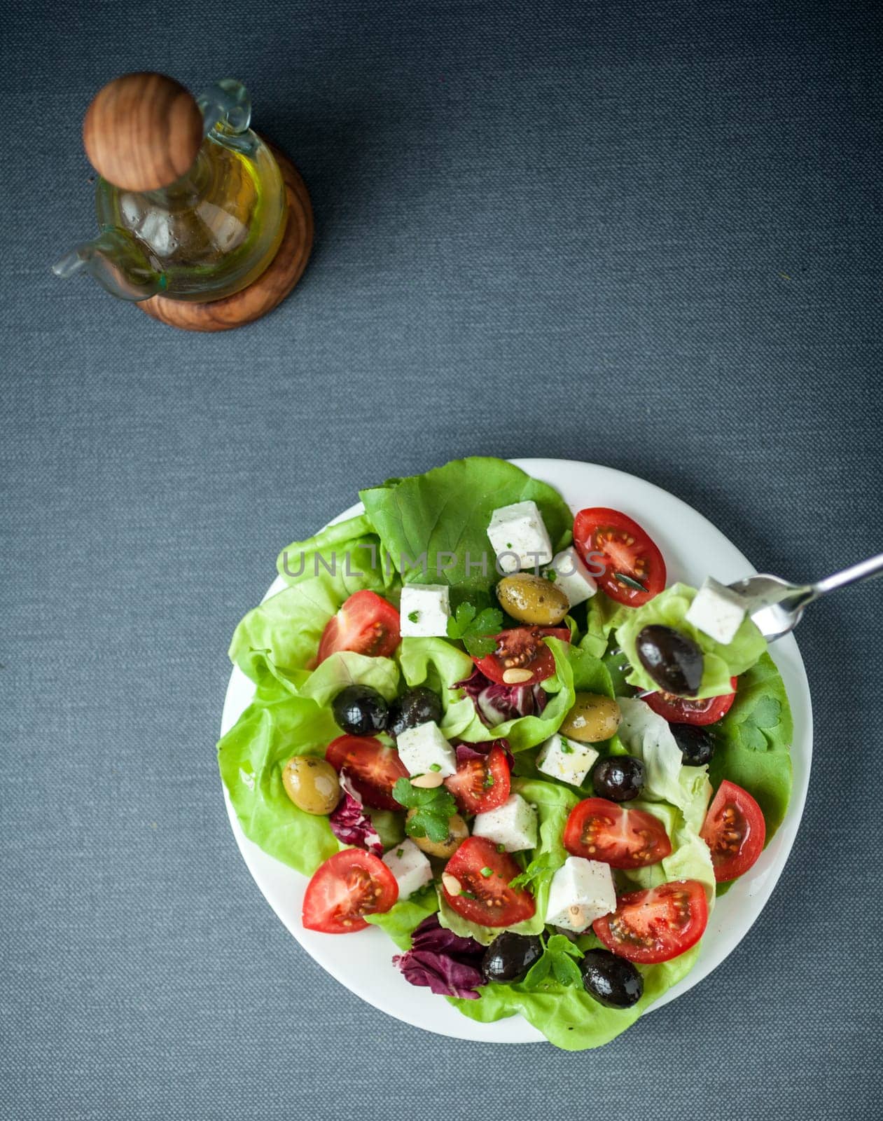 Delicious fresh Mediterranean or Greek salad with lettuce, feta cheese, tomato and assorted olives served with olive oil, overhead view