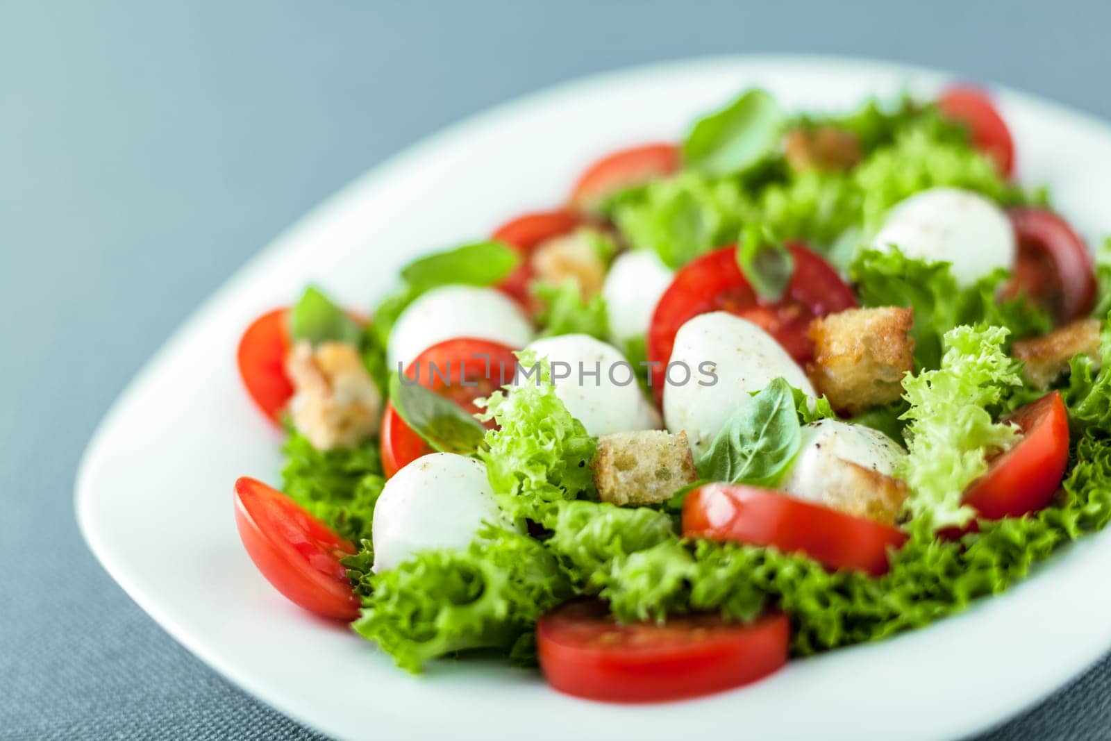 Serving of fresh leafy green salad with mozzarella pearls, tomato and fried golden crunchy croutons, close up low angle view with shallow dof