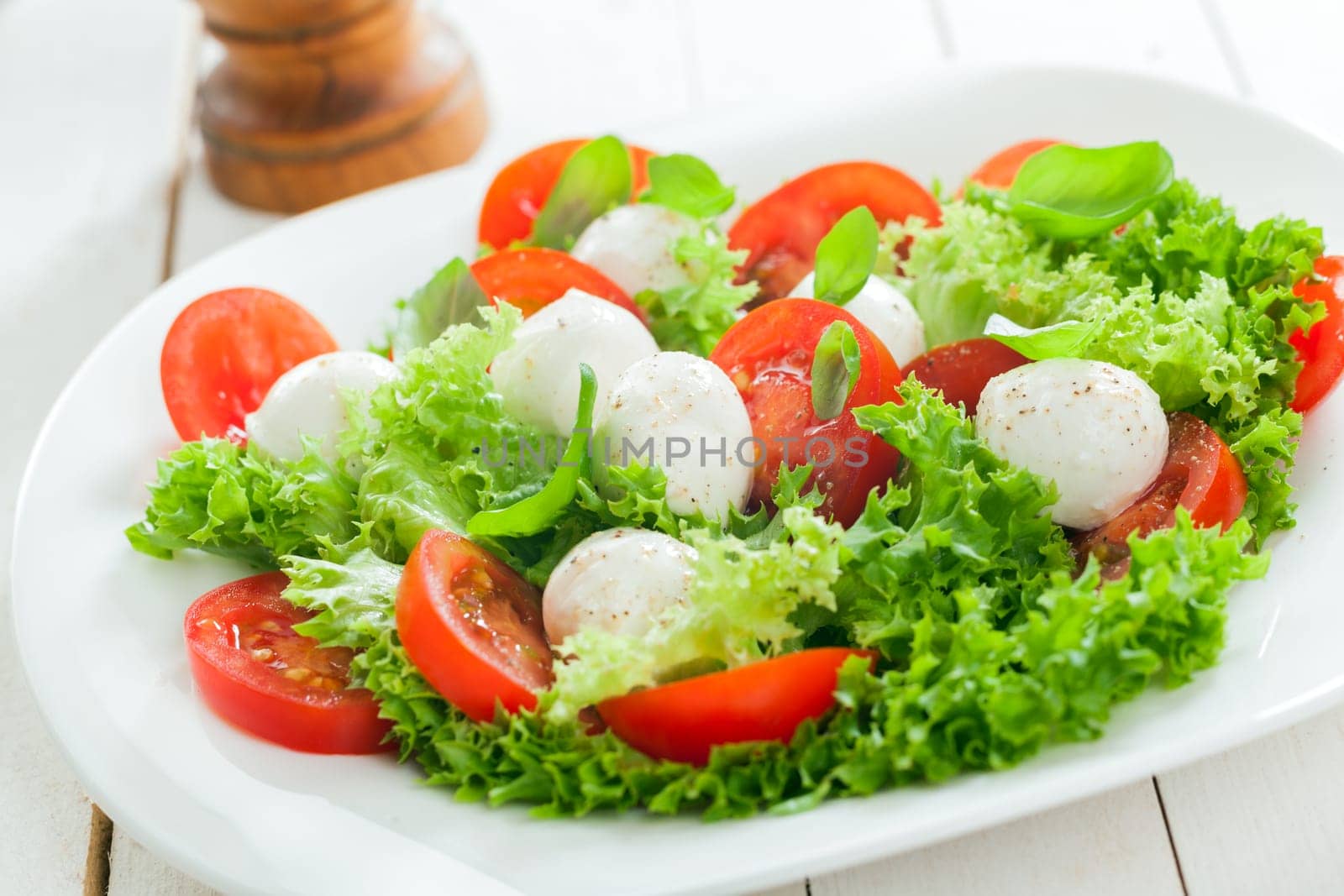 Delicious healthy mozzarella salad with cheese pearls, frilly leafy lettuce, tomato and fresh herbs for tasty Italian cuisine