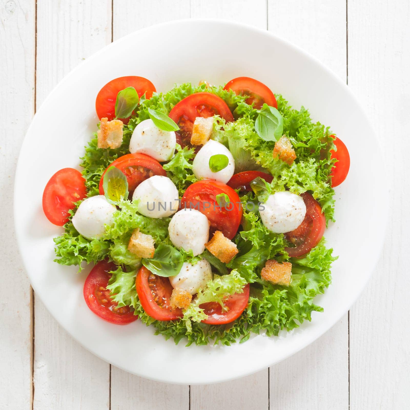 Italian mozzarella cheese and tomato salad with tomatoes and crisp crunchy fried bread cretins, view from above on a plate on white wooden boards, square format