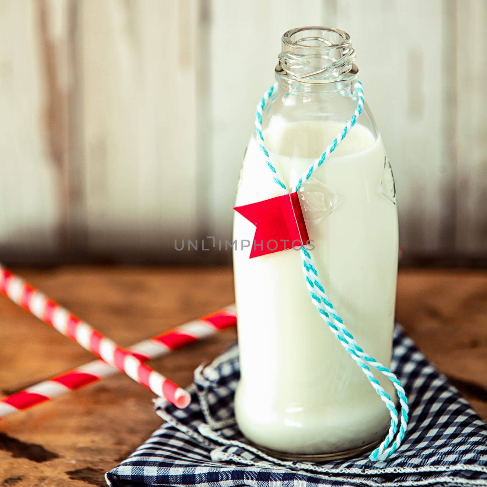 Glass bottle of fresh full cream farm milk with a label attached on a string served with two straws on a rustic checkered blue and white napkin