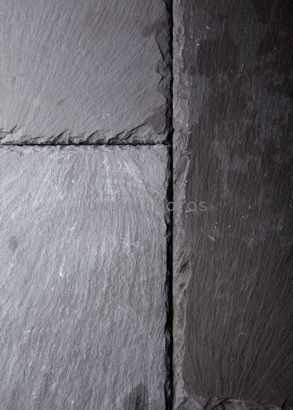 Textured background pattern of natural dark grey slate tiles abutting each other with rough surfaces and slightly chipped edges