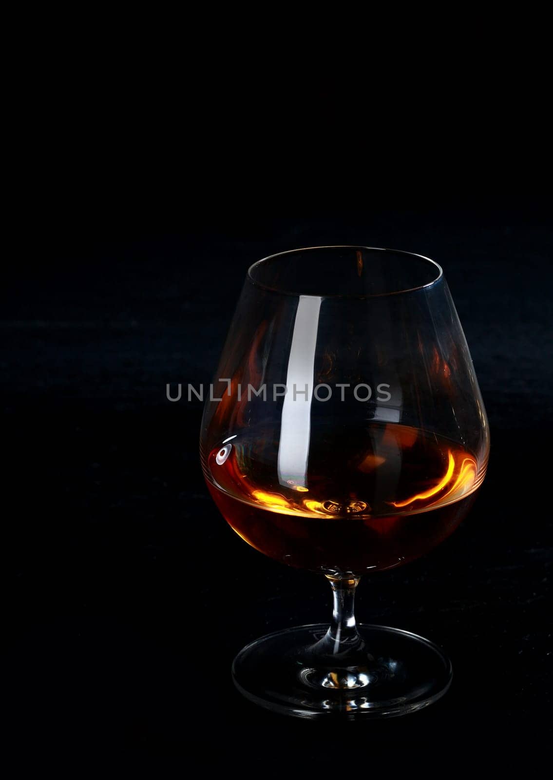 Glowing cognac or brandy in a snifter standing on a dark bar counter in a nightclub in the shadows with vertical copyspace