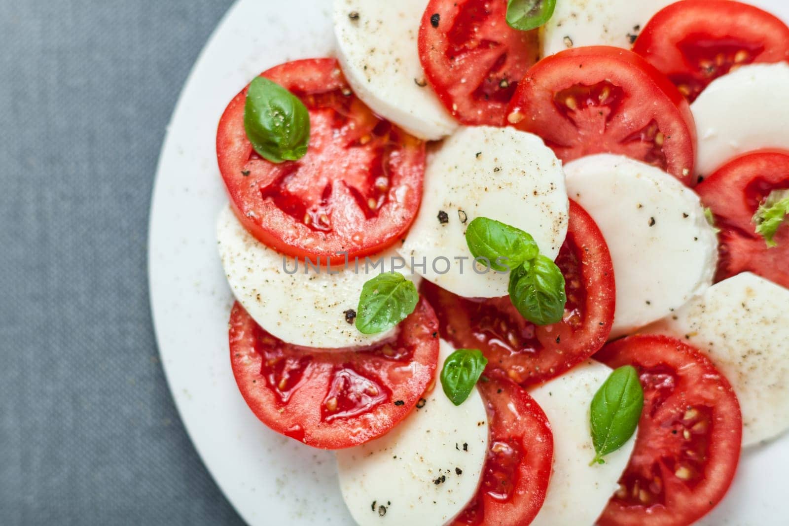 Colorful red and white Italian Caprese salad viewed from above with alternating slices of ripe red tomato and mozzarella cheese seasoned with fresh basil