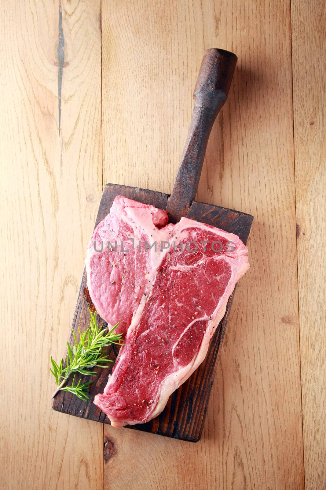 Raw t-bone or porterhouse steak with a sprig of fresh rosemary on a vintage wooden board , overhead view on wood with copyspace