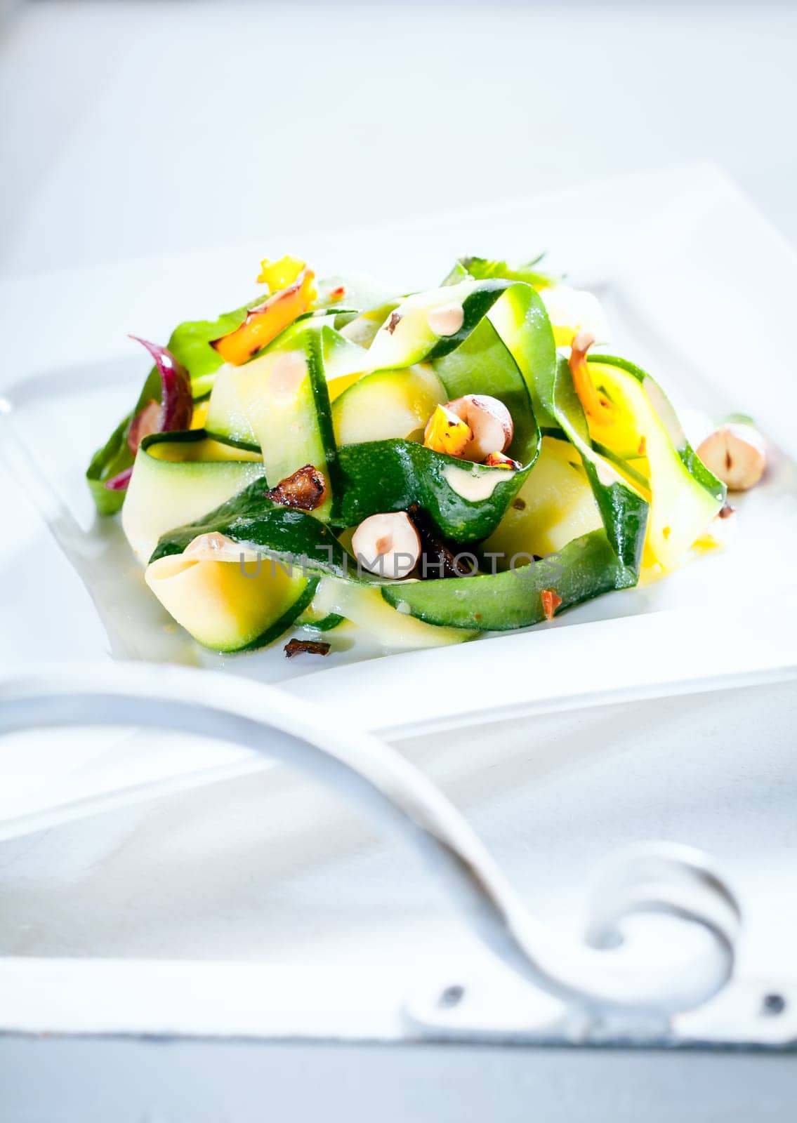 Delicious healthy fresh summer salad served outdoors on a white table in sunlight with the scrolled white metal arm of garden furniture in the foreground