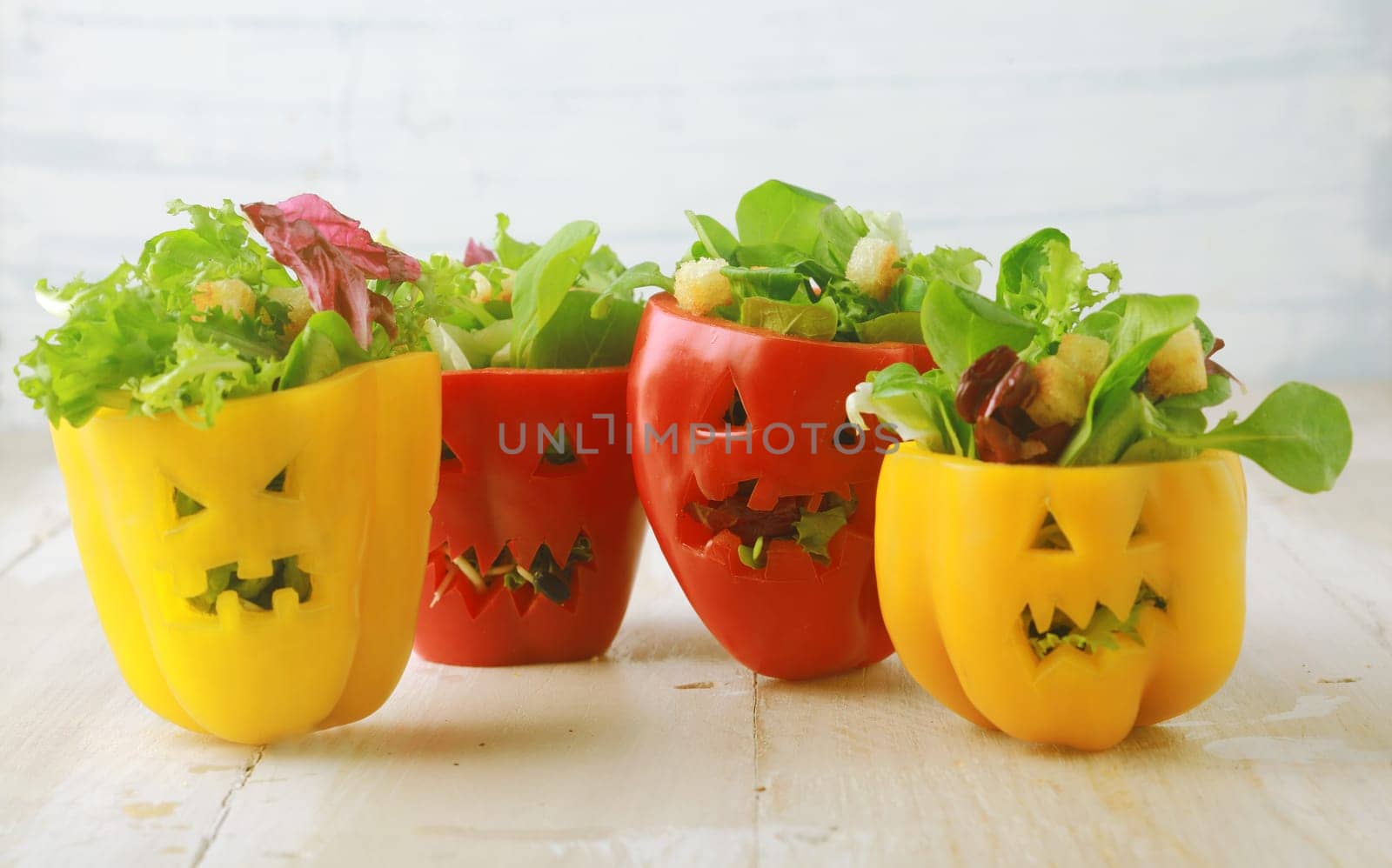 Colorful Halloween food background with colorful healthy stuffed red and yellow sweet bell peppers with cutout faces in the skin like Halloween jack-o-lanterns filled with green salad and cheese