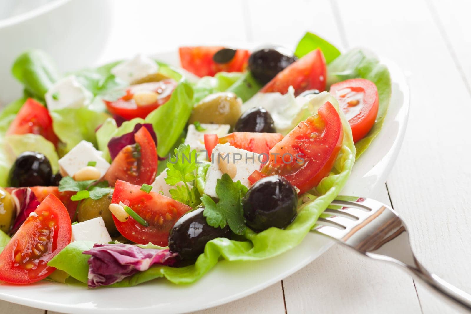 Healthy appetizing Mediterranean salad with fresh tomato, olives, feta cheese, herbs and lettuce, close up view on a plate