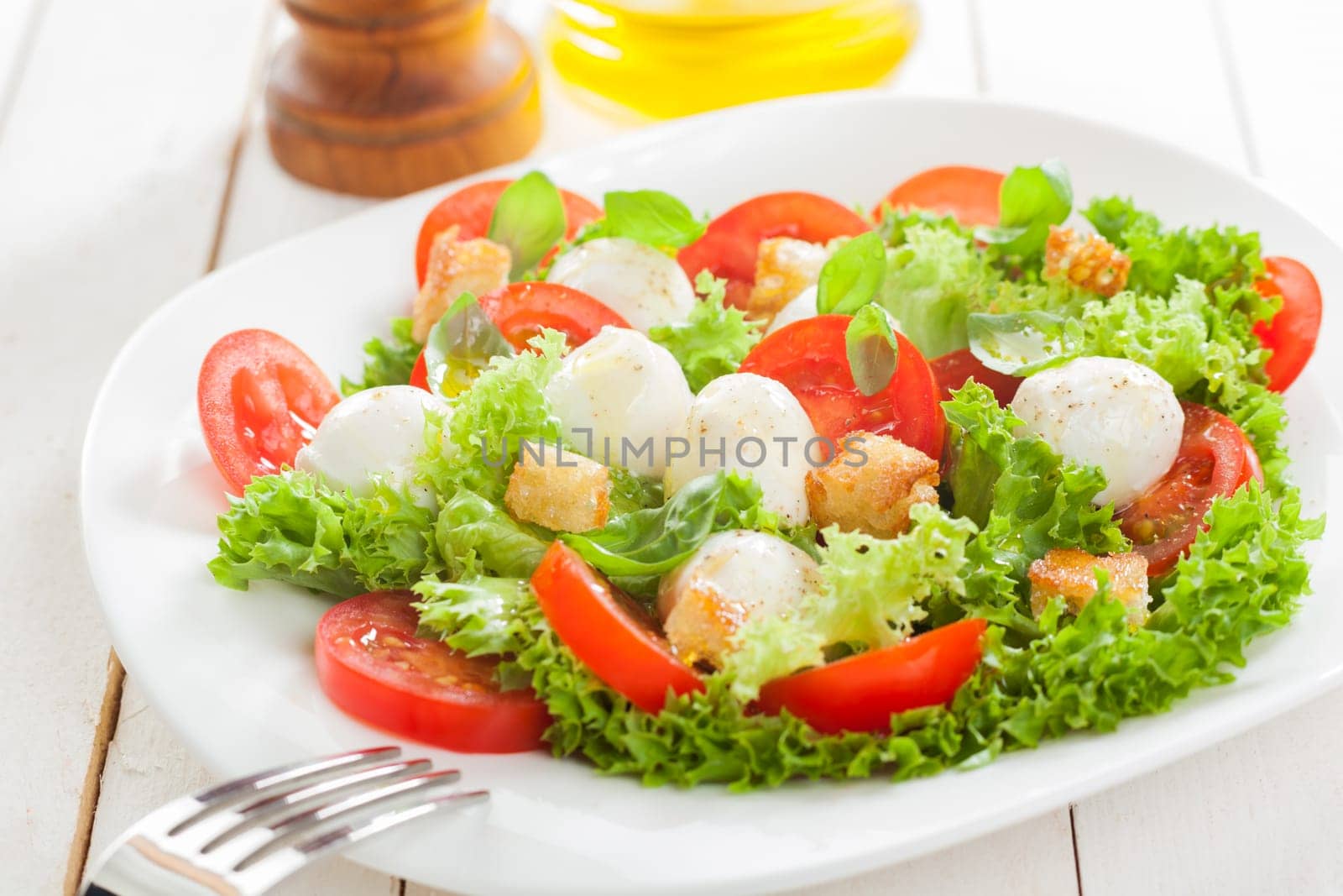 Delicious Italian mozzarella salad with crunchy fried bread croutons, sliced fresh tomato herbs and frilly lettuce served on a plate on white wooden boards