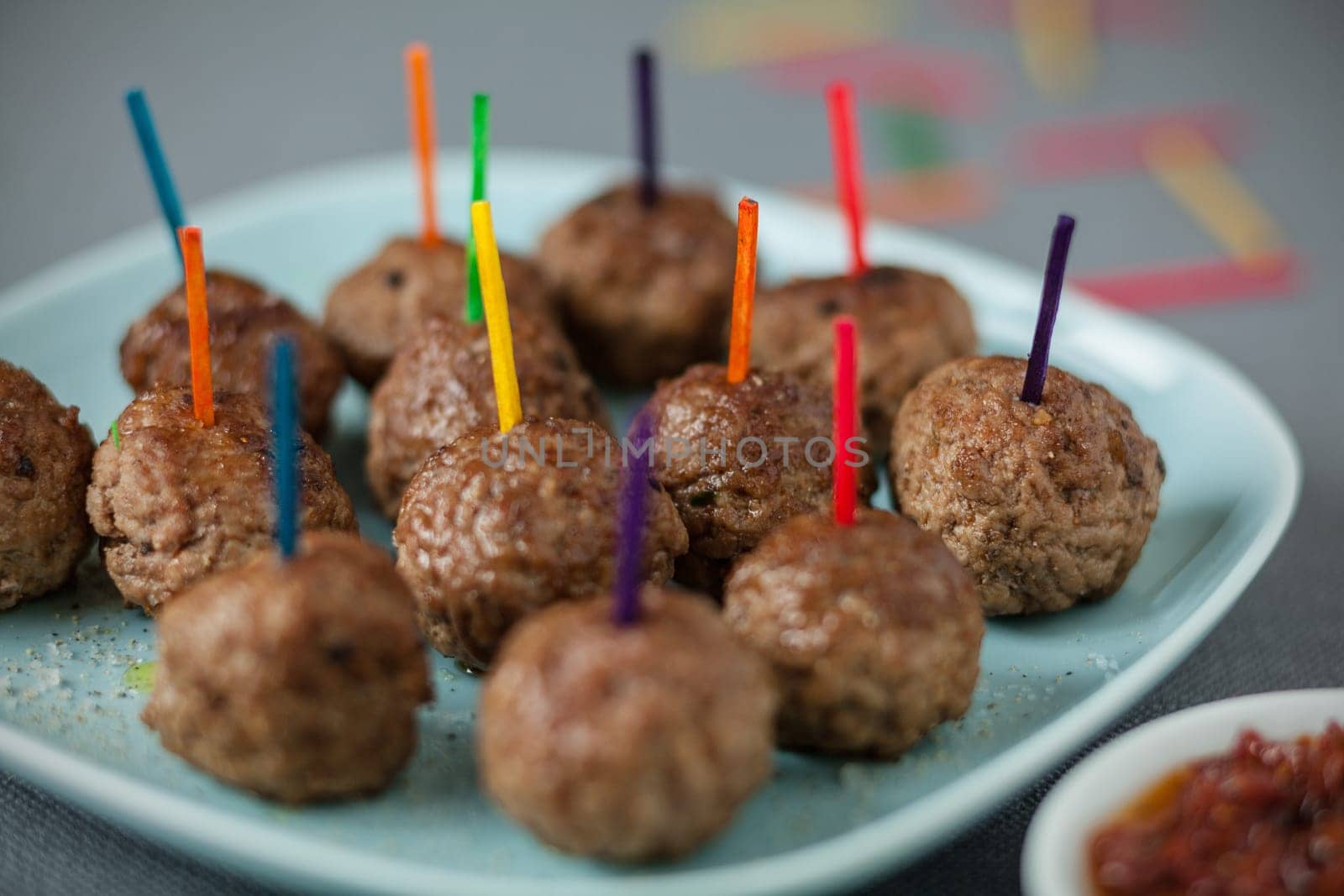 Plate of tasty spicy savoury meatballs for party snacks with colorful toothpicks for dipping in a bowl of piquant sauce