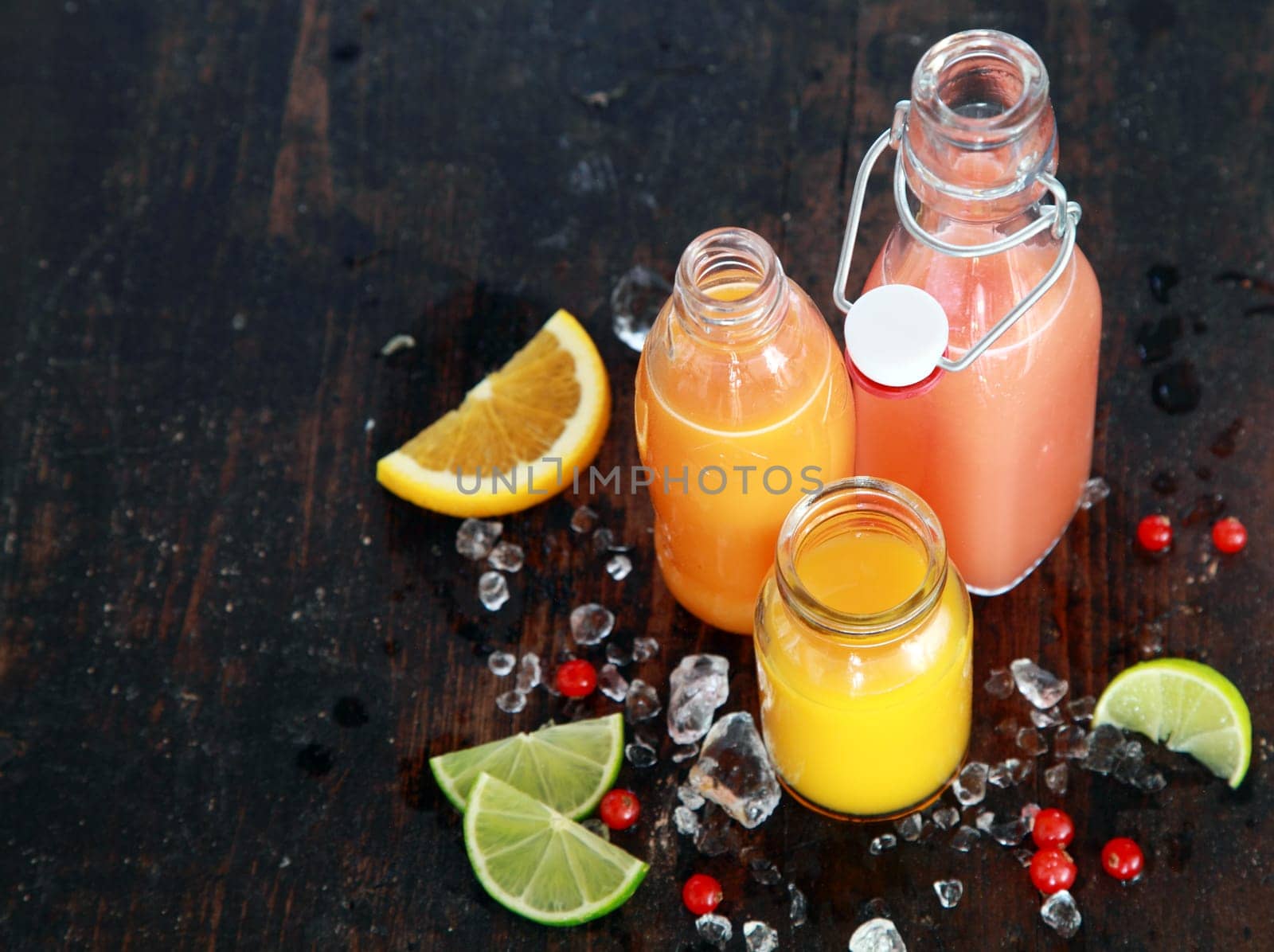 Preparing tasty healthy summer fruit juices in glass bottles with slices of fresh orange, lemon, lime and cranberries, viewed high angle on a dark rustic wooden surface with copyspace