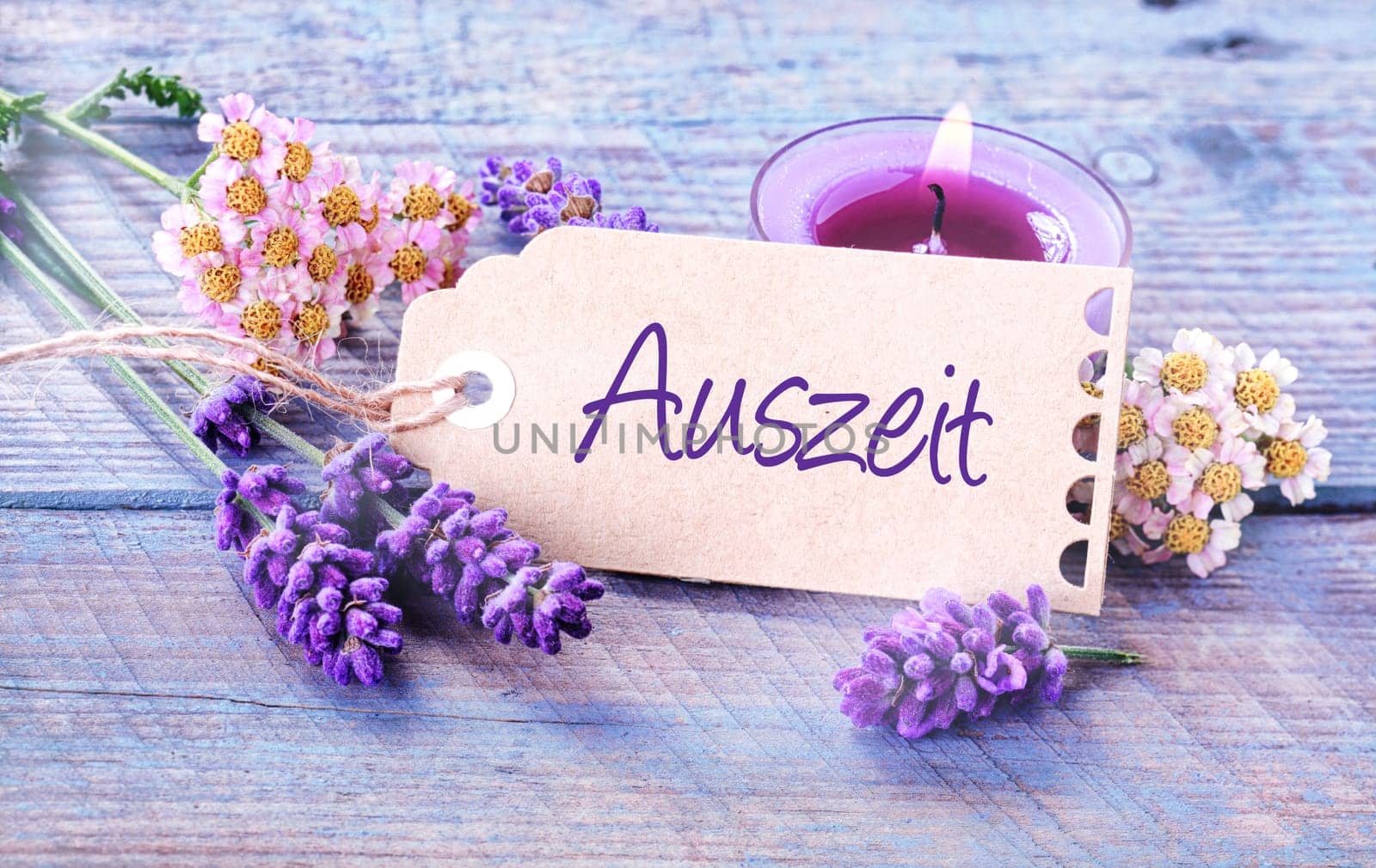 Auszeit- Relaxation - rustic floral background with dainty lavender spikes and flowers with a burning aromatherapy candle surrounding a label with the word - Auszeit - on pale blue wooden boards