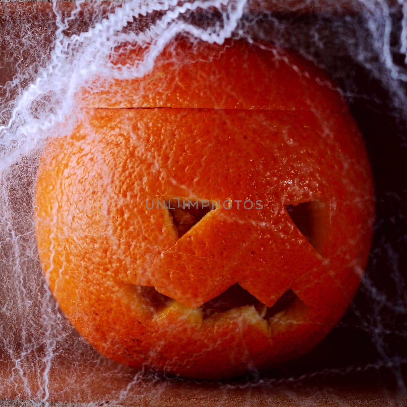 Colorful fresh orange Halloween lantern carved with a traditional jack-o-lantern face covered in spooky eerie cobwebs for a creative rustic handicraft Halloween background