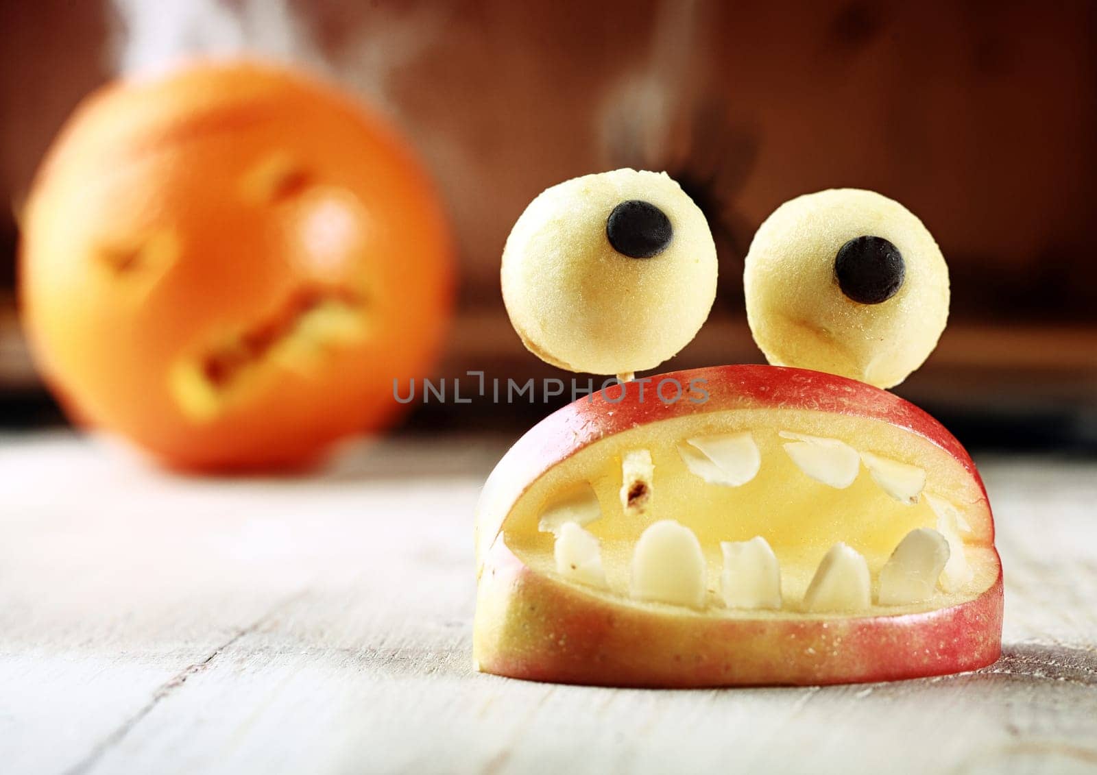 Cute homemade Halloween apple decoration of an open mouth with teeth topped with googly dough eyes on toothpicks for a scary but healthy favor to give children trick-or-treating