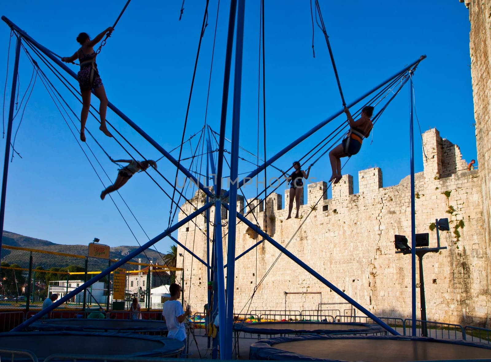 TROGIR, CROATIA - AUGUST 13, 2014 Girls have fun jumping on the trampoline with rubber bands near medieval Kamerlengo castle, famous landmark in Trogir