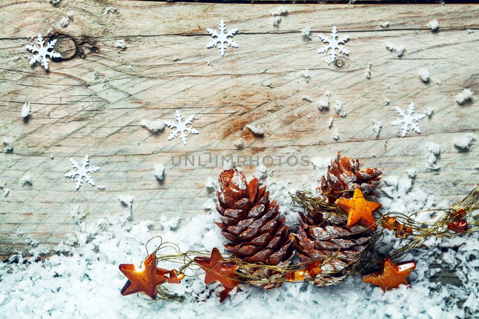 Christmas Noel background with dried pine cones draped in a garland of stars nestling on cold winter snow with a wooden background with snowflake decorations and copyspace