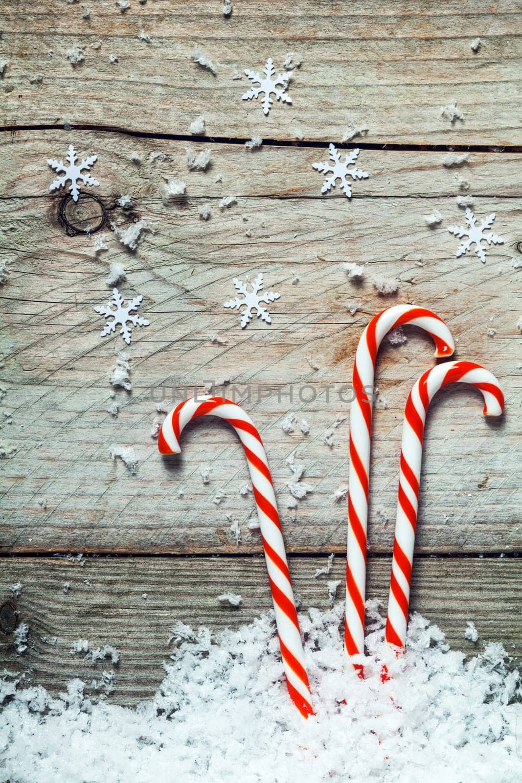 Colorful striped red and white Xmas candy canes with scattered winter snow lying on old cracked dried wooden boards with copyspace