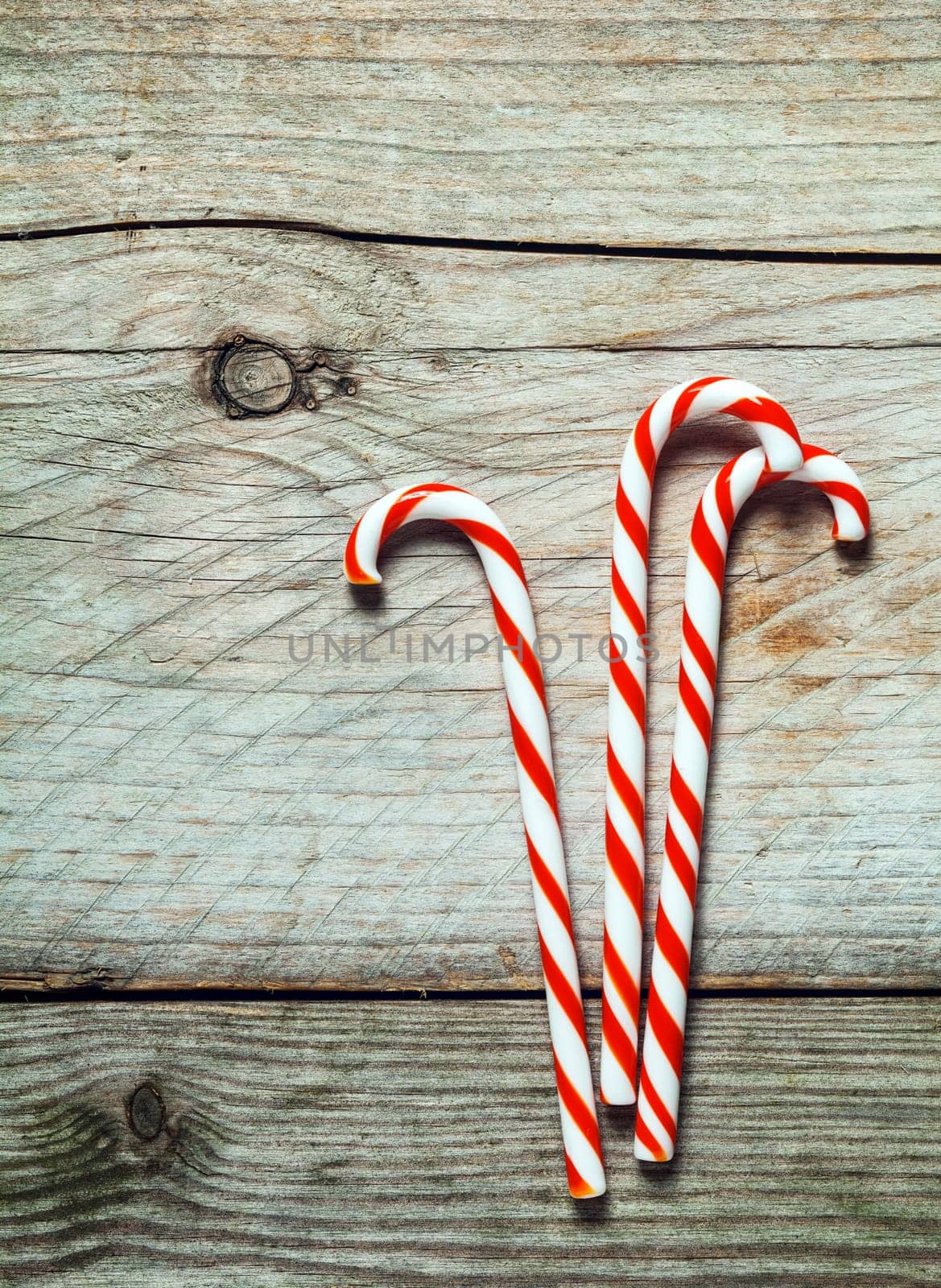 Colorful red and white striped Xmas candy canes on a rustic wooden background with copyspace for your seasonal Christmas greeting or invitation