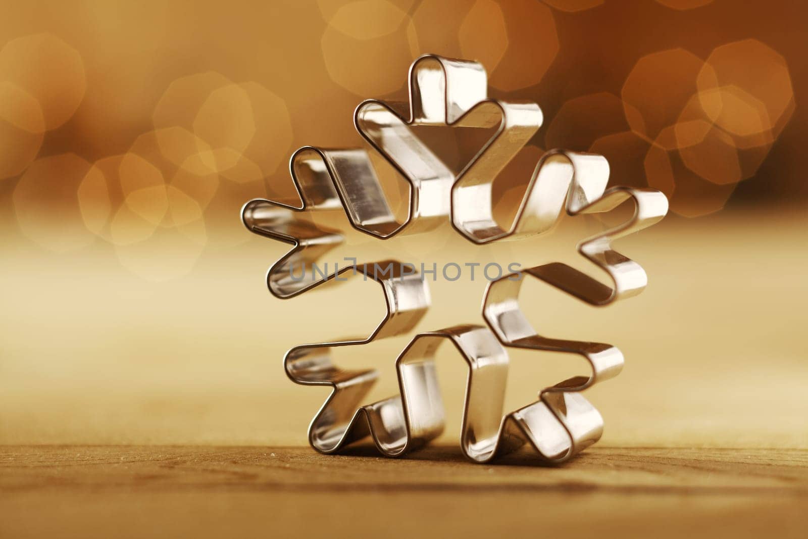 Snowflake Christmas background with a shiny aluminium cookie cutter standing upright on a sepia background with a faint bokeh of party lights and copyspace for your seasonal greeting