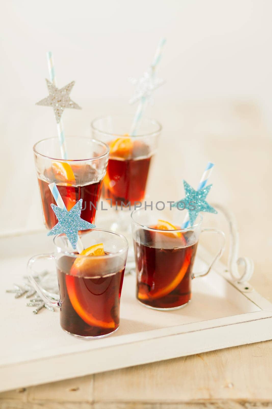 Four glasses of festive Christmas punch with spices and orange slices served with decorative straws with blue glitter stars